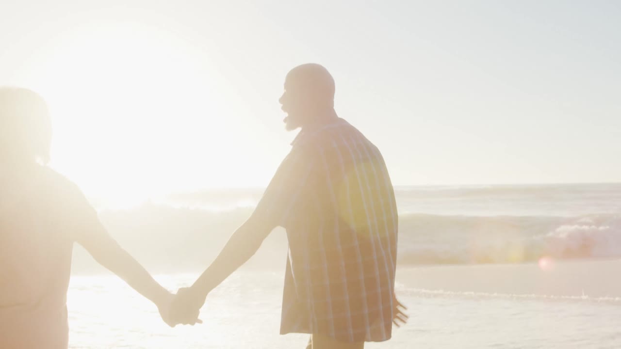 웃는 아프리카계 미국인 부부가 손을 잡고  ⁇ 은 해변에서  ⁇ 고 있습니다.