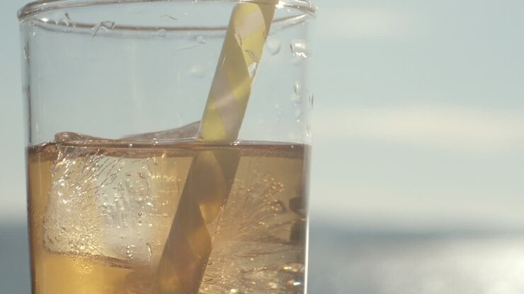 Close up Tilt up shot of a glass filled with ice and orange transparent liquid, Sun Lens flares, Slowmo