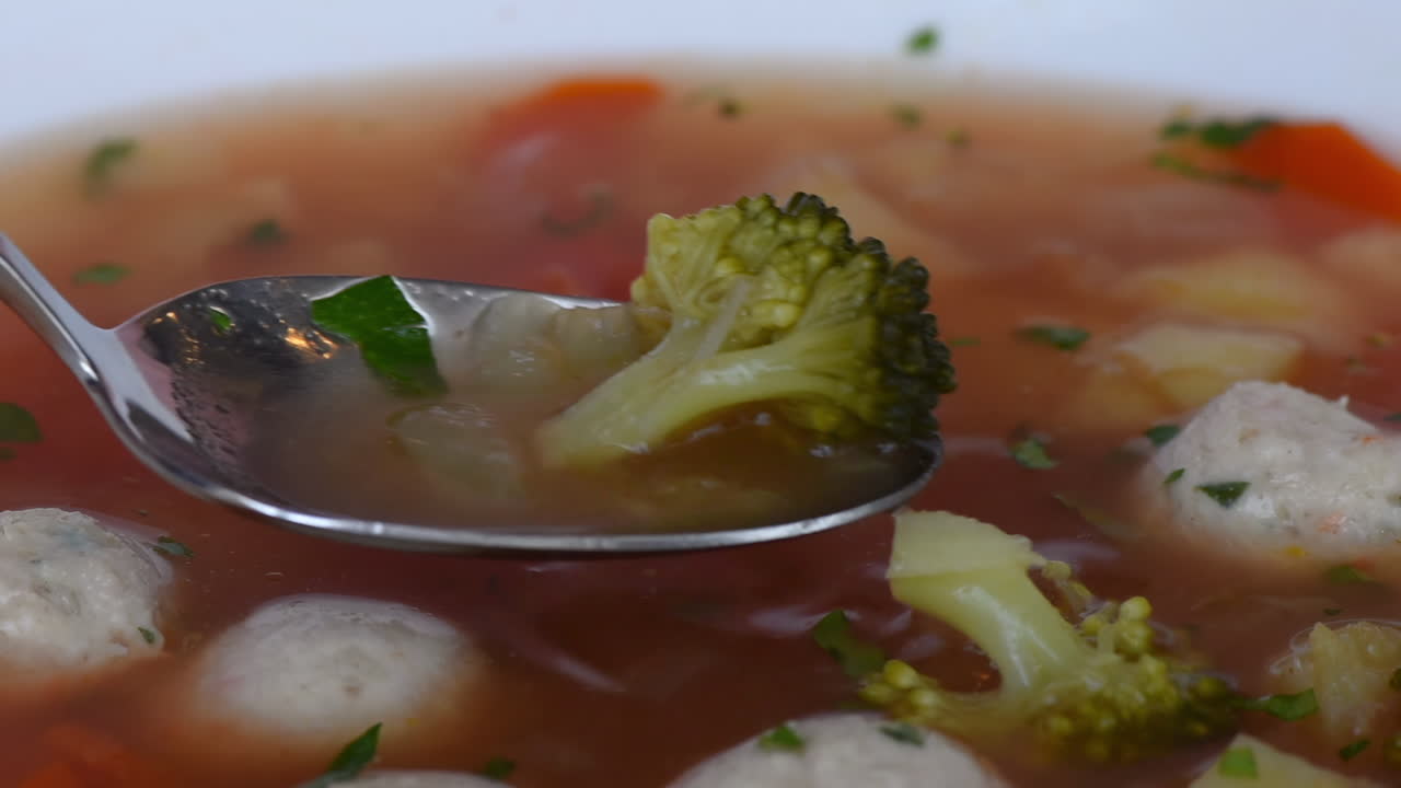 Close of a spoon picking up a meatball soup in a white plate