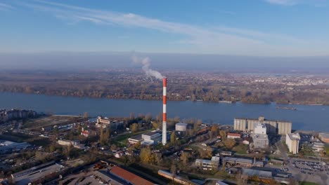 Imágenes-Aéreas-Que-Ascienden-Y-Se-Centran-En-Una-Chimenea-En-La-Ciudad-De-Belgrado,-Serbia,-Con-El-Río-Danubio-Al-Fondo.