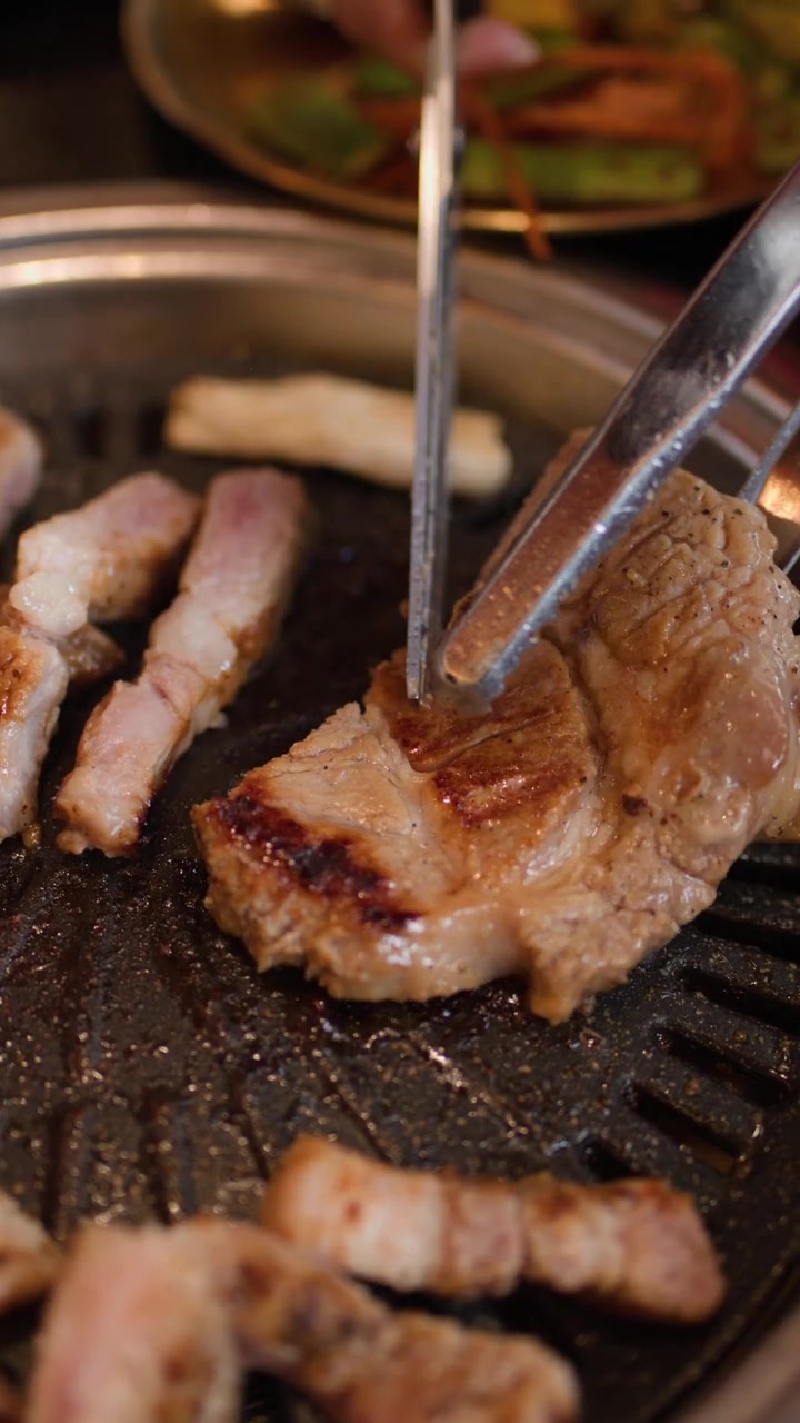 Tampilan dekat perut babi yang dipanggang di atas barbekyu meja, diiris dengan gunting dalam pencahayaan restoran yang hangat.