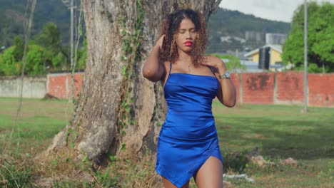 una joven con el cabello rizado en un vestido azul corto está disfrutando de un parque tropical en la isla de trinidad