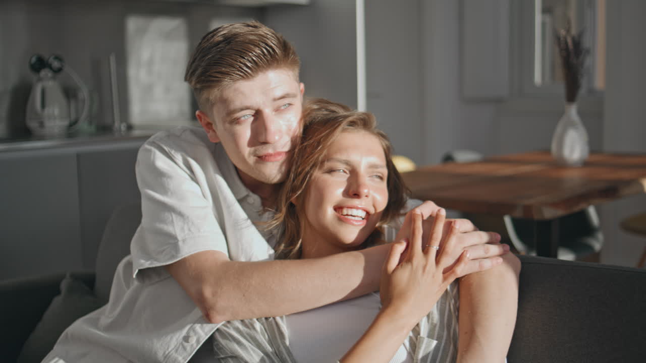 Romantic spouses talking sofa in sunlight. Closeup happy lovers cuddling home
