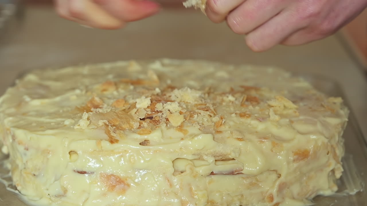 Close up of a woman's hands decorating a homemade cake covered in creamy frosting on a kitchen counter