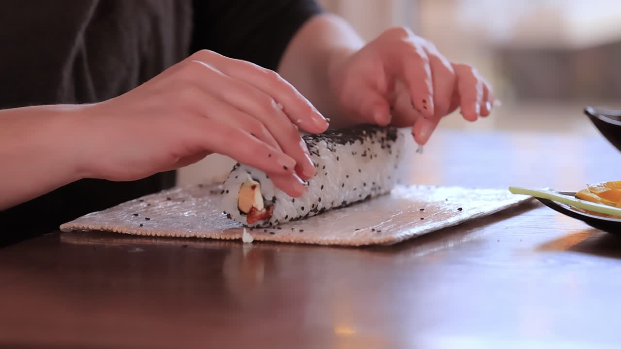 hacer sushi en la cocina de casa. manos de mujer enrollando sushi casero.