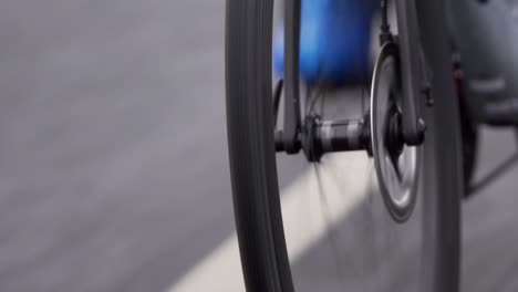 close up clip of narrow front wheel of a road bike, showing grip and tread of the tire and rotation, with blue cycling shoes and white road markings in the background