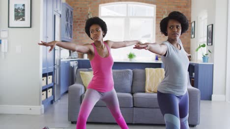 Happy-african-american-mother-and-daughter-doing-yoga-in-living-room,-stretching
