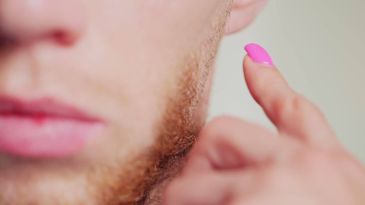 Closeup of red-bearded man getting beard trimmed by woman using electric clipper