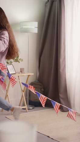 vertical video of woman at home hanging up american stars and stripes flag bunting for party celebrating 4th july independence day