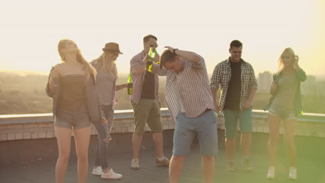 a company of six young people threw a party on the roof with beer. three young men and two young girls are dancing in plaid shirts. young blonde dances in the foreground in denim shorts and denim jacket.