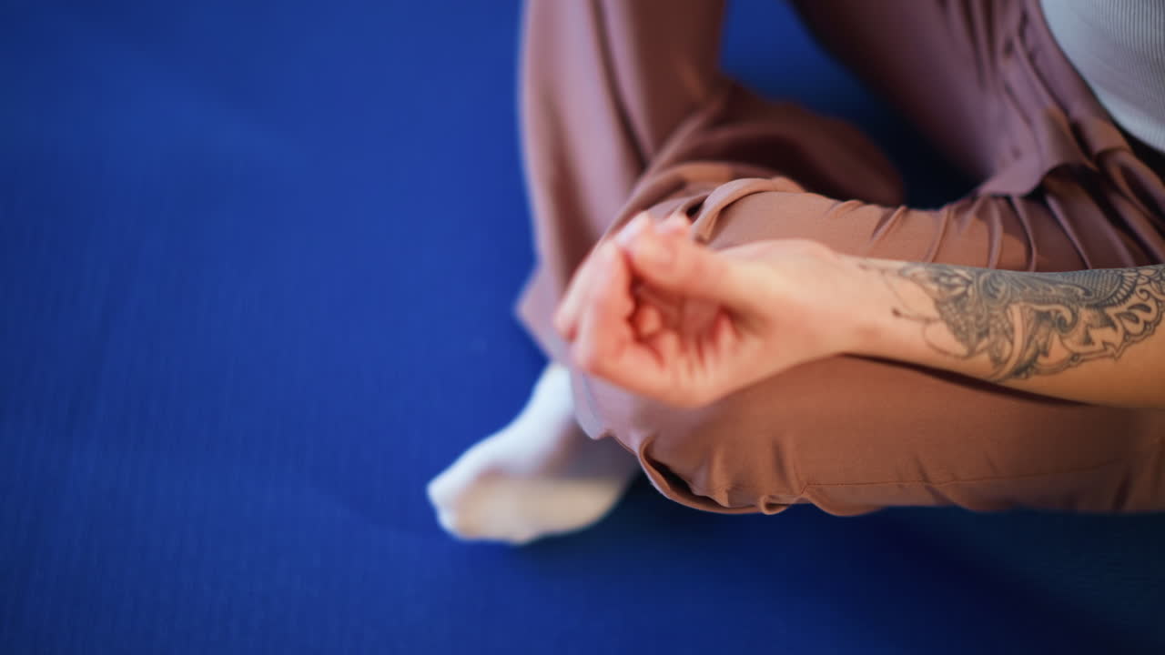 Tattooed Hand Forming Mudra On Blue Mat During Seated Meditation Mindful Practitioner Takes Focused Breath, Indoor Calm, Gentle Posture And Quiet Home Studio Atmosphere For Centering Practice