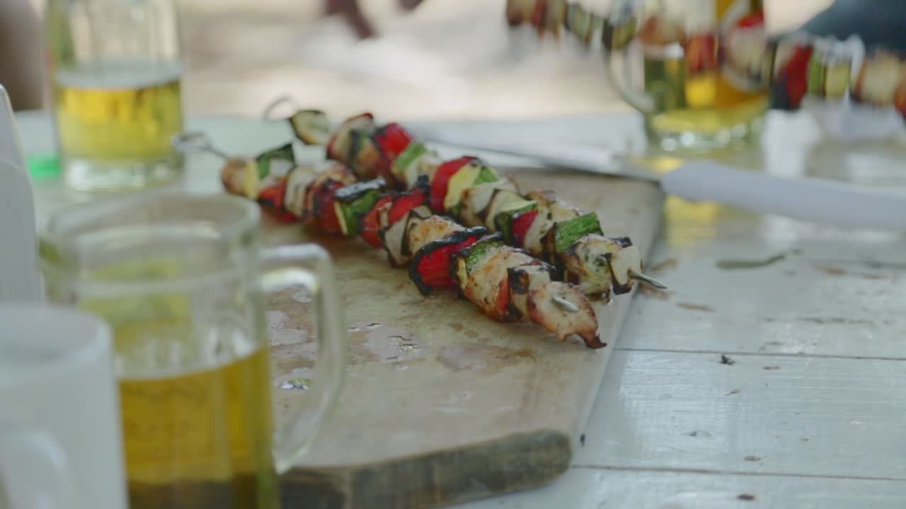 cerrar las manos agarrar y comer pinchos de pollo de la mesa de picnic con cervezas