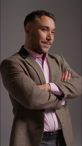 vertical video studio portrait of smiling mature male teacher wearing jacket folding arms standing against grey background