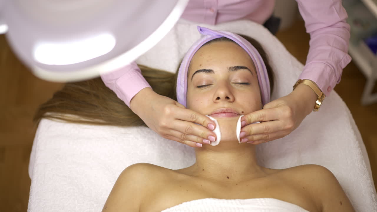 Woman receiving a facial cleansing treatment with cotton pads at a beauty salon