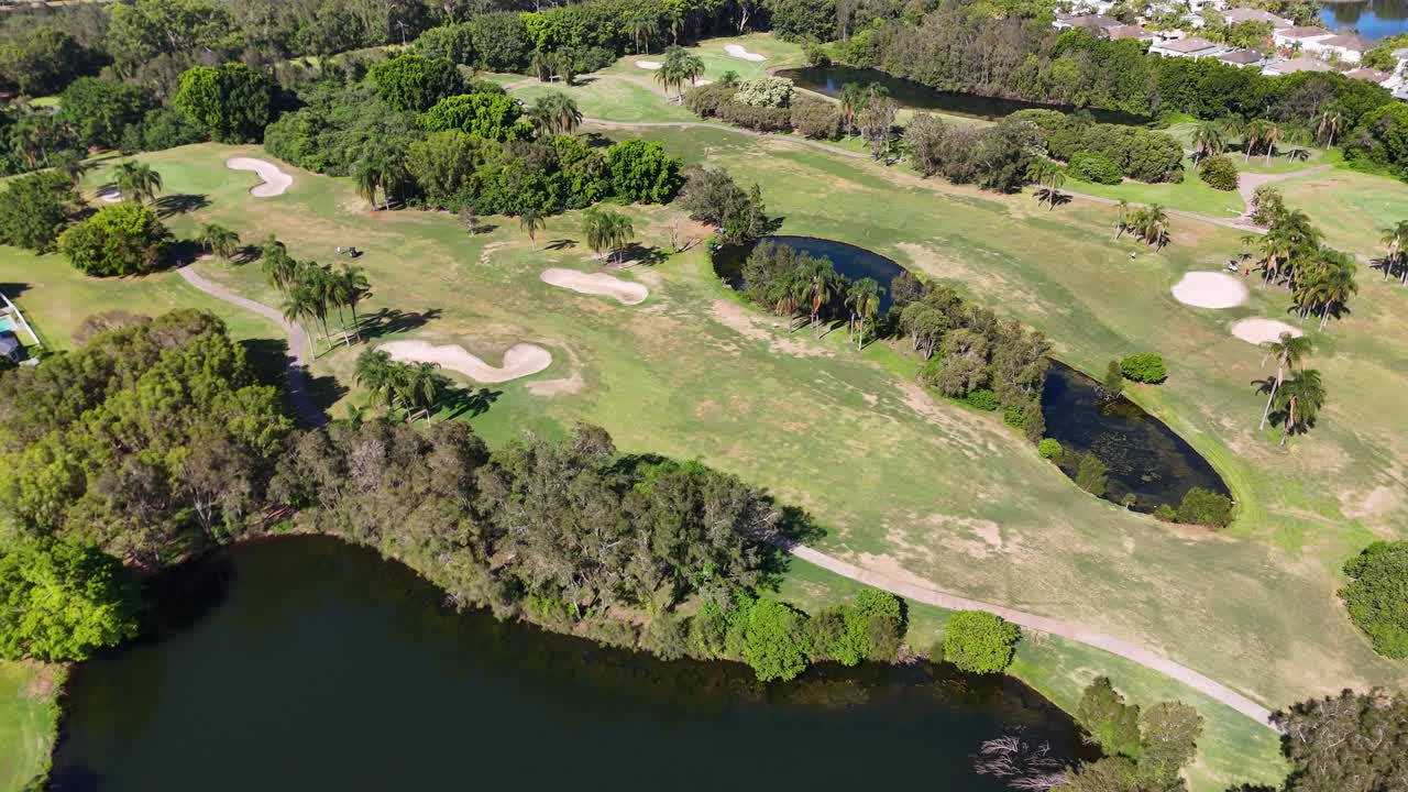 Sunny drone flyover of lush golf course fairway with sand bunkers, lake, and trees