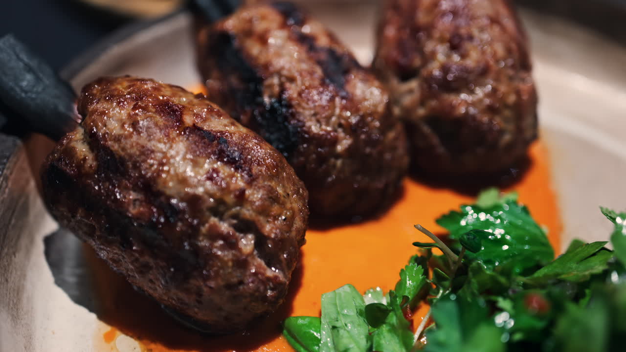 Three grilled meat skewers on charcoal sticks served on a plate with an orange sauce