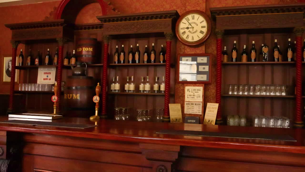 A vintage bar setting with wooden shelves, bottles, and a clock, captured in warm lighting at Sovereign Hill, Ballarat
