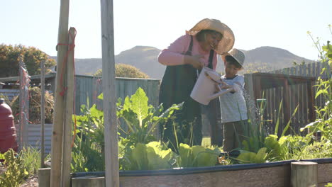 Abuela-Birracial-Mayor-Y-Nieto-Regando-Plantas-En-Un-Jardín-Soleado,-Cámara-Lenta,-Espacio-De-Copia