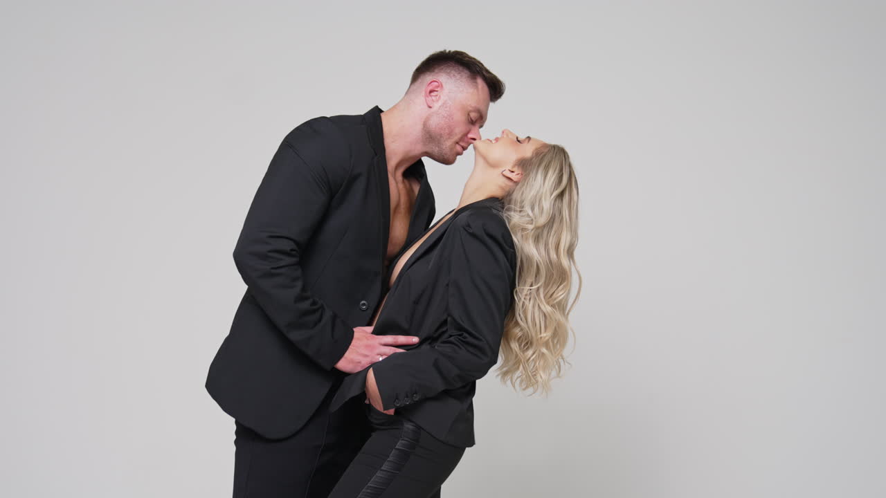 Caucasian couple wearing black jackets and trousers. Happy passionate couple footage in studio. White backdrop.