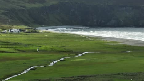 kiteboarding down narrow river near rough ocean waves, green meadows, lush green beautiful landscape, achill island, ireland