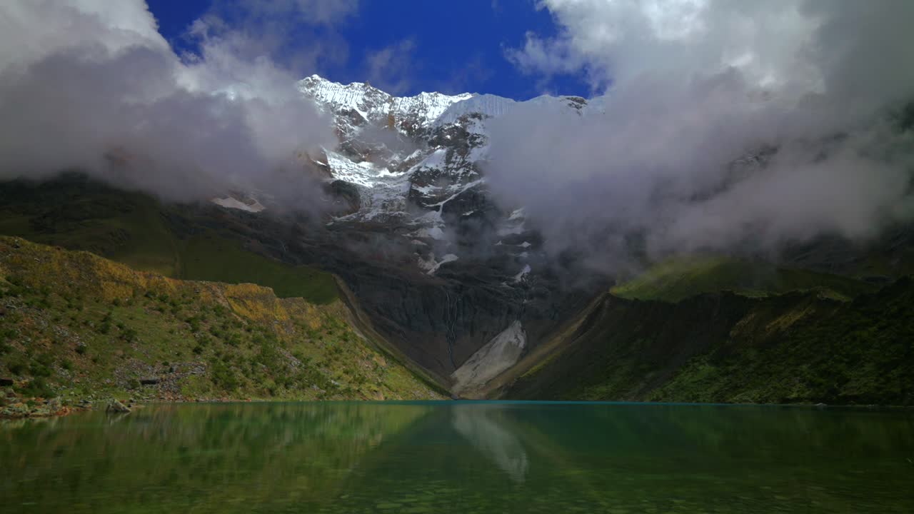 Lago glaciale Laguna Humantay del Perù, riva rocciosa del Lago Humantay, Ande peruviane, Monte Humantay, vista paesaggistica della natura del Perù, cime innevate, strato di nebbia e nuvole, mattina soleggiata e nuvolosa, destinazione turistica.