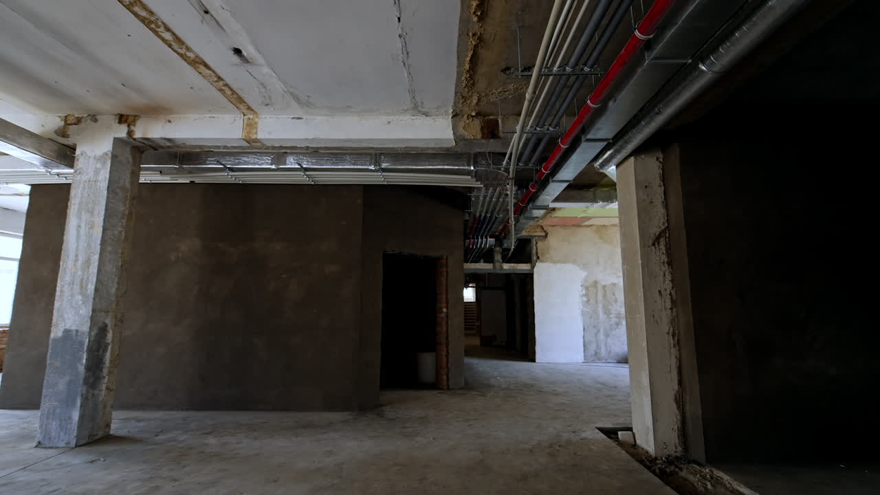 Inside the spacious room with unfinished walls, ceiling and floor. Low angle view at the pipes on the ceiling of the premise. Renovation concept.
