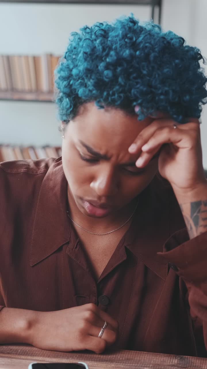 Young puzzled african american woman upset reading sms on phone sits at table