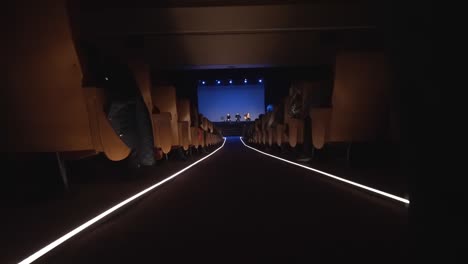 Actress-slowly-enters-the-darkened-theatre,-walks-down-the-central-aisle-to-the-stage