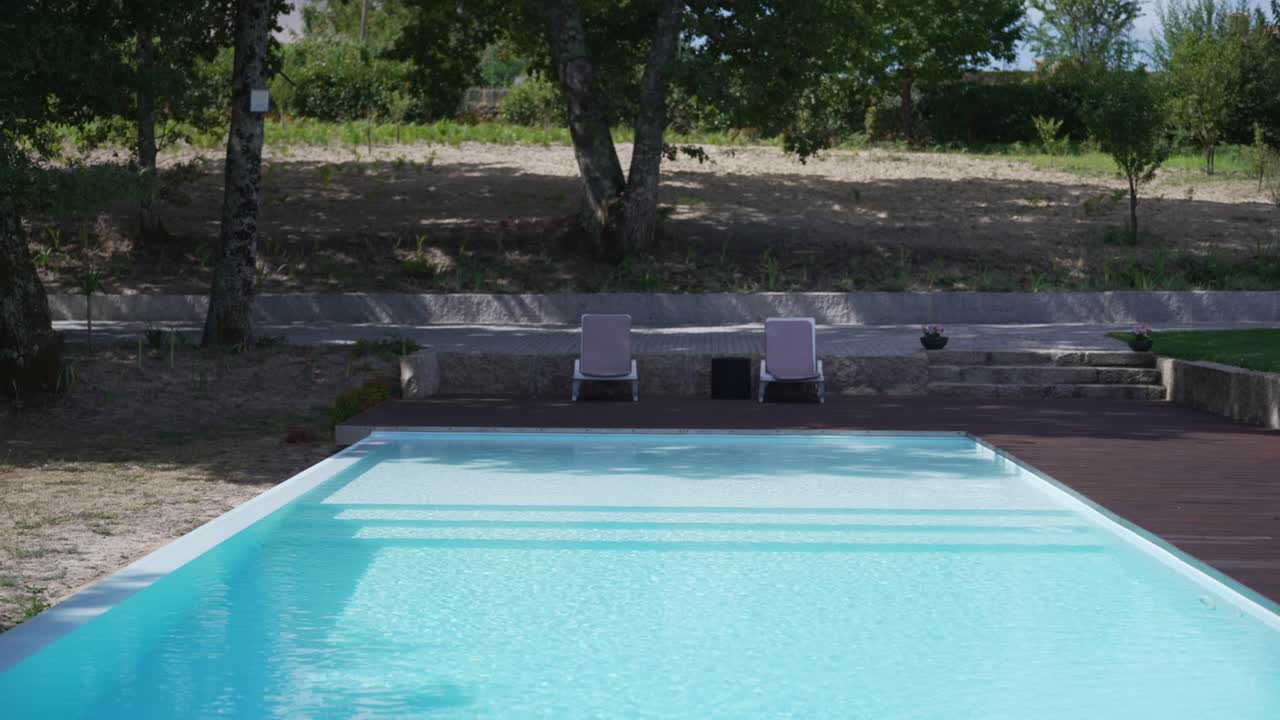 Vista serena de una piscina azul clara rodeada de naturaleza y tumbonas al sol