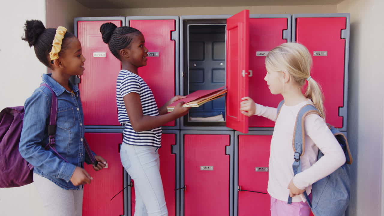 In school, three girls using lockers and organizing books in hallway