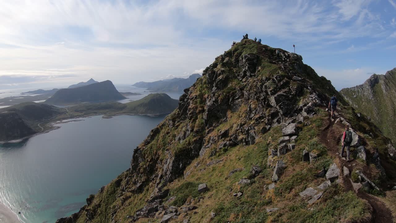 algunos excursionistas caminan por el sendero hasta la cima de la montaña mannen, con vistas a la playa de haukland y los fiordos al fondo en lofoten, noruega