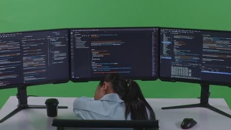 back view of tired asian woman developer sleeping while write code with multiple computer screens in green screen studio