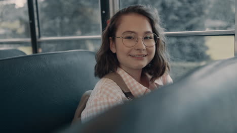 smiling school girl sitting at bus window in glasses. student looking camera.