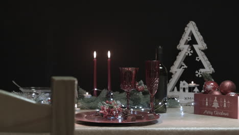 Man-places-a-red-Christmas-tree-ball-on-a-decorated-table-in-a-dark-room-with-a-chair-in-foreground