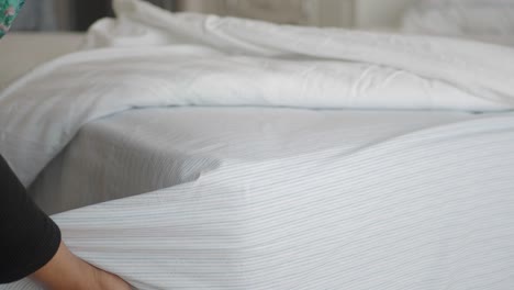 woman making a bed with white and blue striped sheets