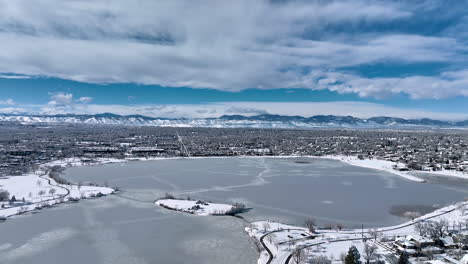 aerial drone shot circling moving over a frozen sloan lake, denver during winter storm showing rocky mountains in background