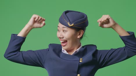 close up of asian woman air hostess smiling and flexing her bicep while standing in the green screen background studio