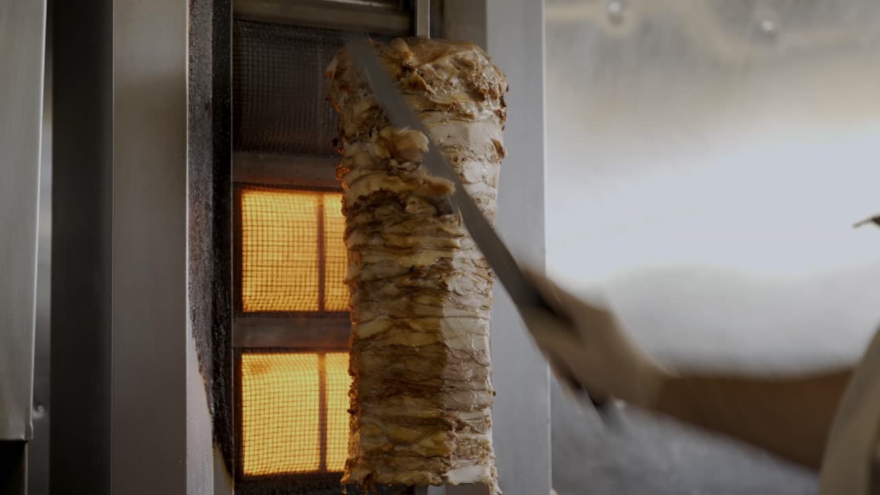 chef cortando rebanadas de un gran pincho de shawarma de pollo colgado en la parrilla