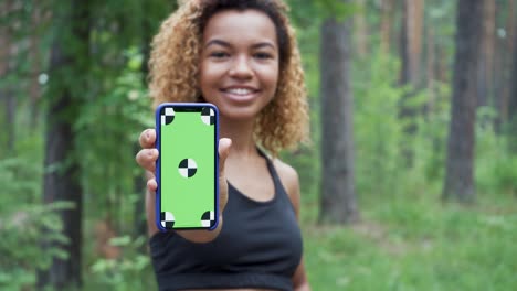 black young woman using her smartphone in a break from jogging and shows green screen to the camera