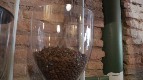 pouring bag of freshly roasted coffee beans into glass jar on top of coffee grinder