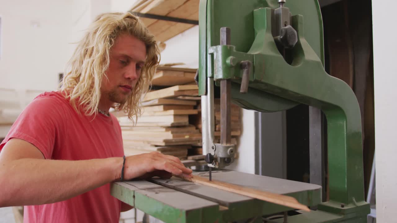 fabricante de tablas de surf masculino caucásico trabajando en su estudio y haciendo una tabla de surf de madera