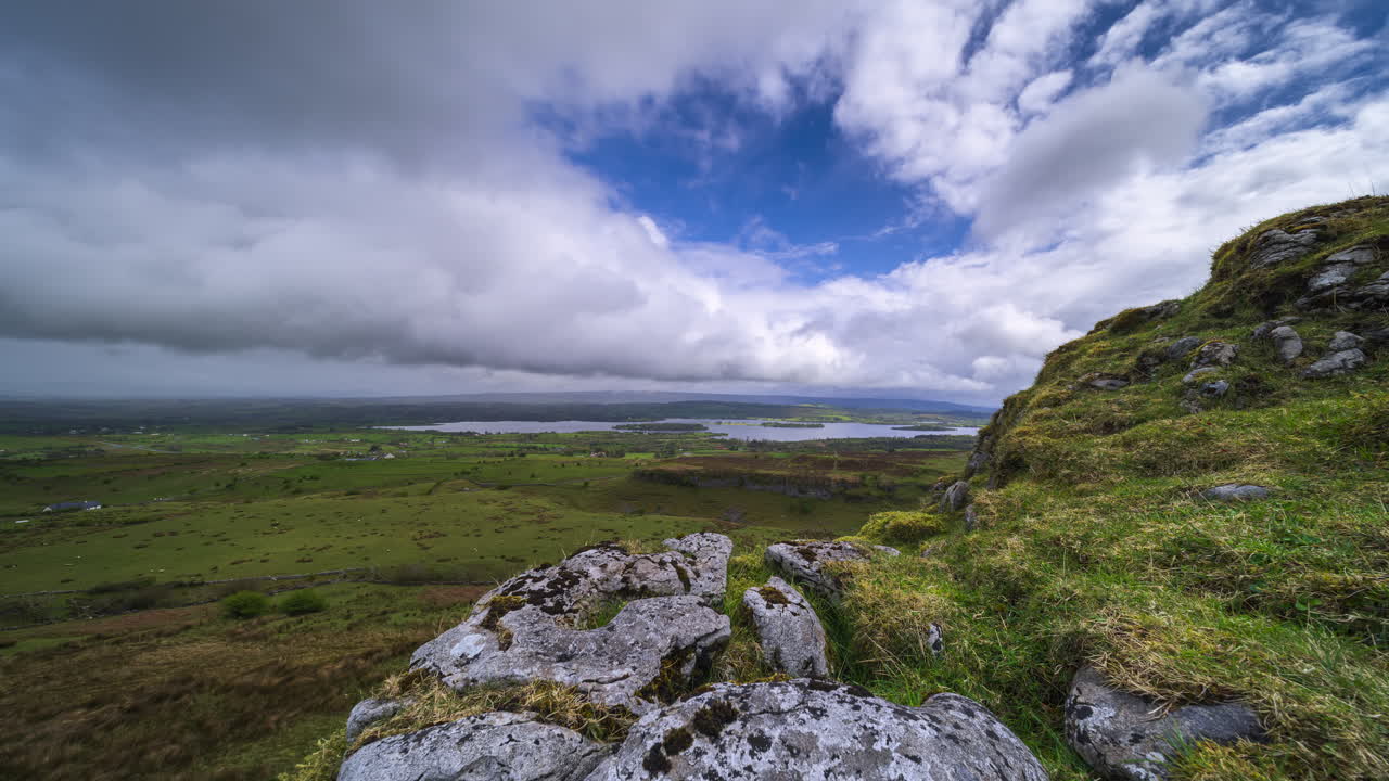 Timelapse di una valle rurale con formazione rocciosa in primo piano e tempesta di pioggia in arrivo, colline e lago in lontananza in una giornata primaverile visti da Carrowkeel, nella contea di Sligo, in Irlanda
