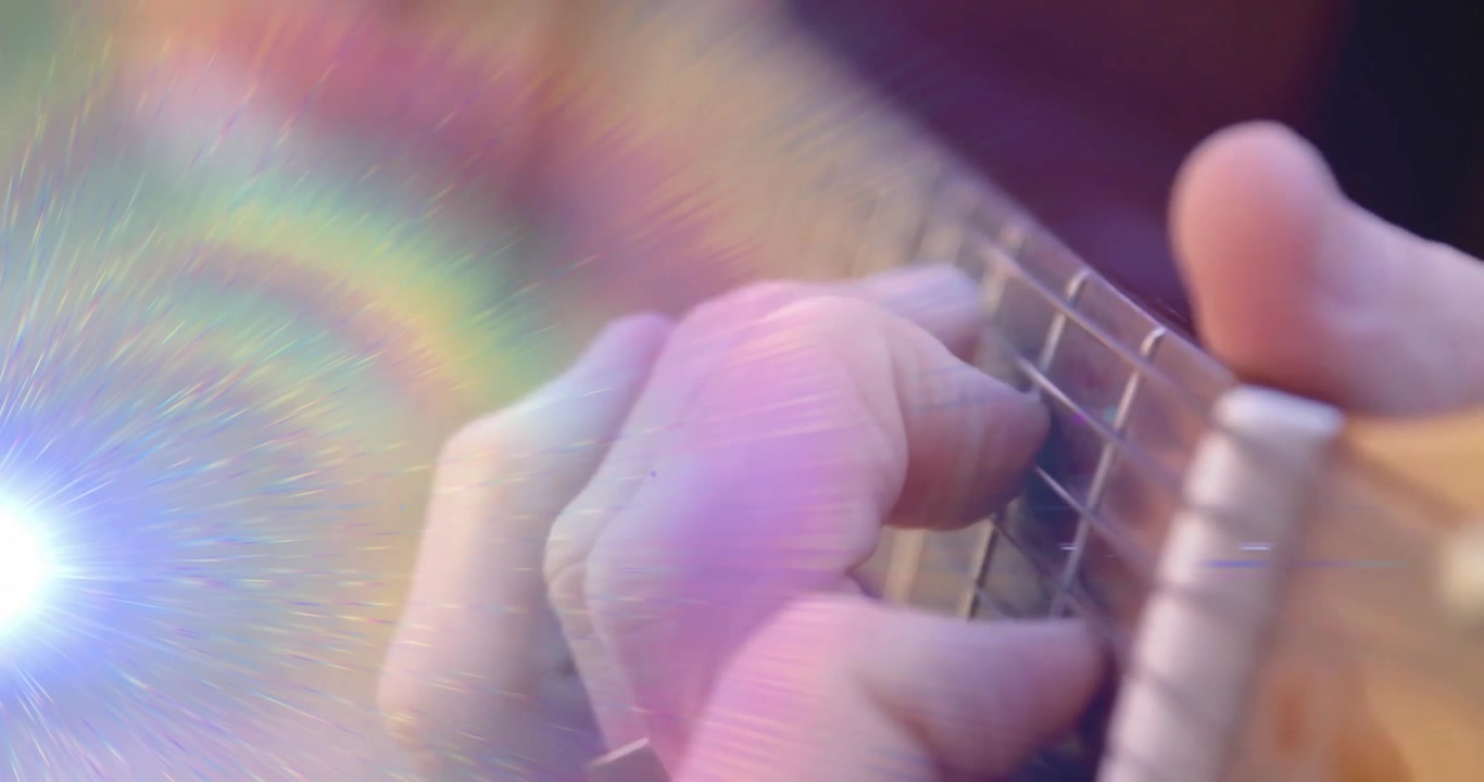 Musician's right hand approaching guitar under prism lighting rainbow flares and plucking melody