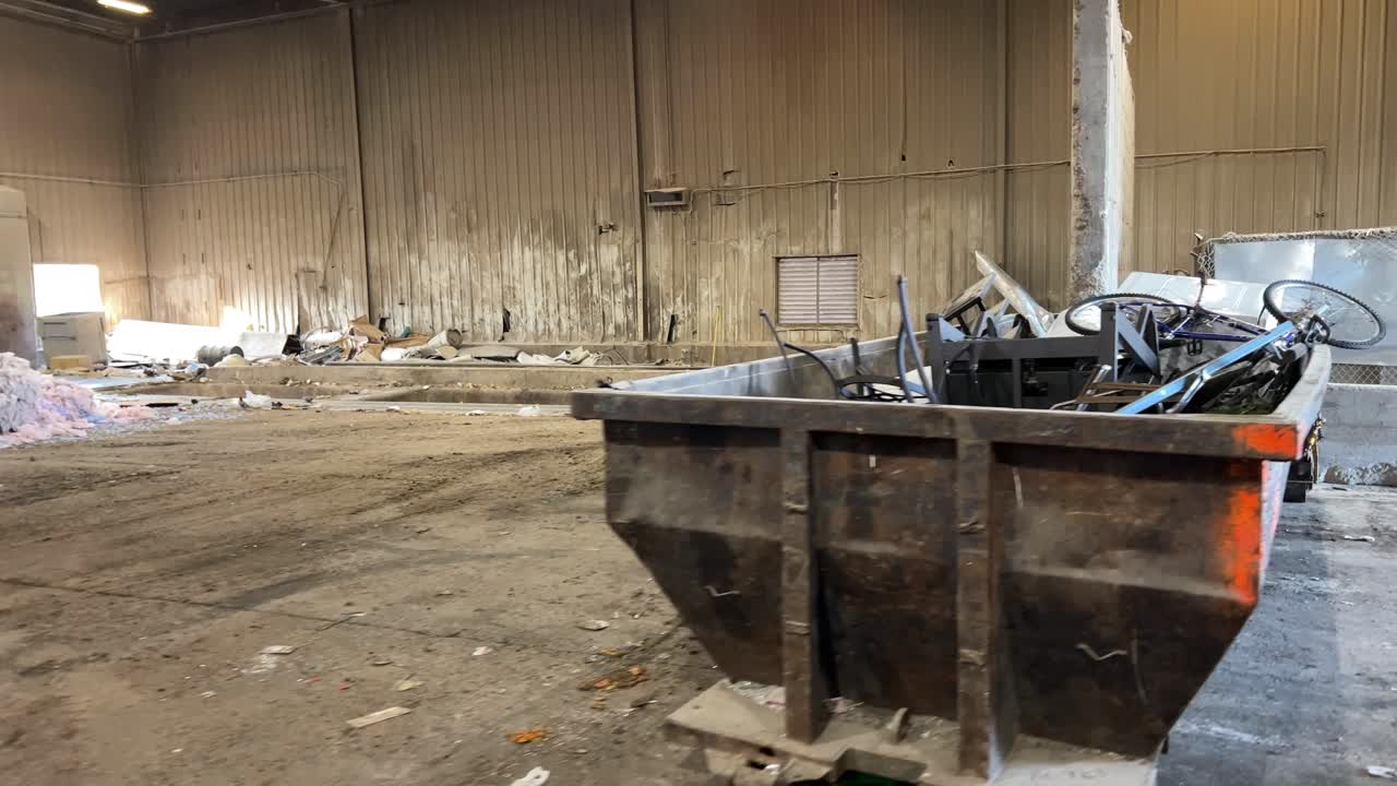 Slow pan from right to left looking at a dumpster full of scrap metal then moving into a large building
