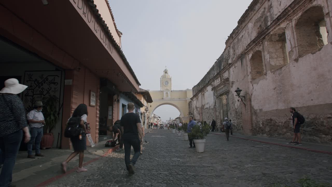panorámica rápida hacia abajo del famoso arco en antigua, guatemala con gente caminando por la calle