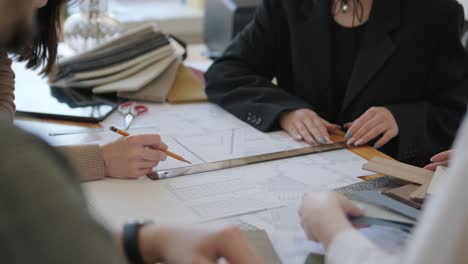 over-the-shoulder view of design professionals focused on architectural blueprints, with fabric samples and tools on the table, during a detailed project discussion