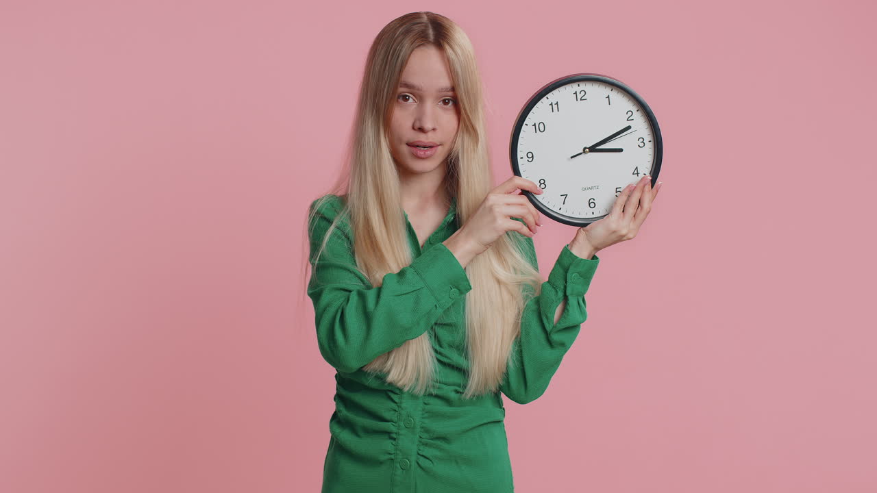 Smiling woman showing time on wall office clock ok thumb up approve pointing finger at camera