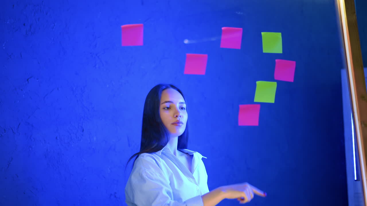 Creative woman stacks bright notes. A young woman is creatively placing sticky notes on a blue wall, forming a heart shape, showcasing artistic expression