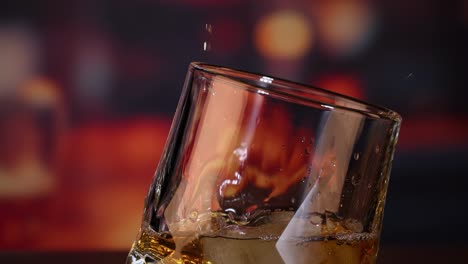 Close-up of amber liquid being poured into a tilted glass containing ice cubes.