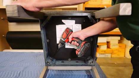 A-furniture-repair-handy-man-uses-a-power-drill-to-loosen-the-bolts-on-the-underside-of-a-wooden-oak-dining-chair